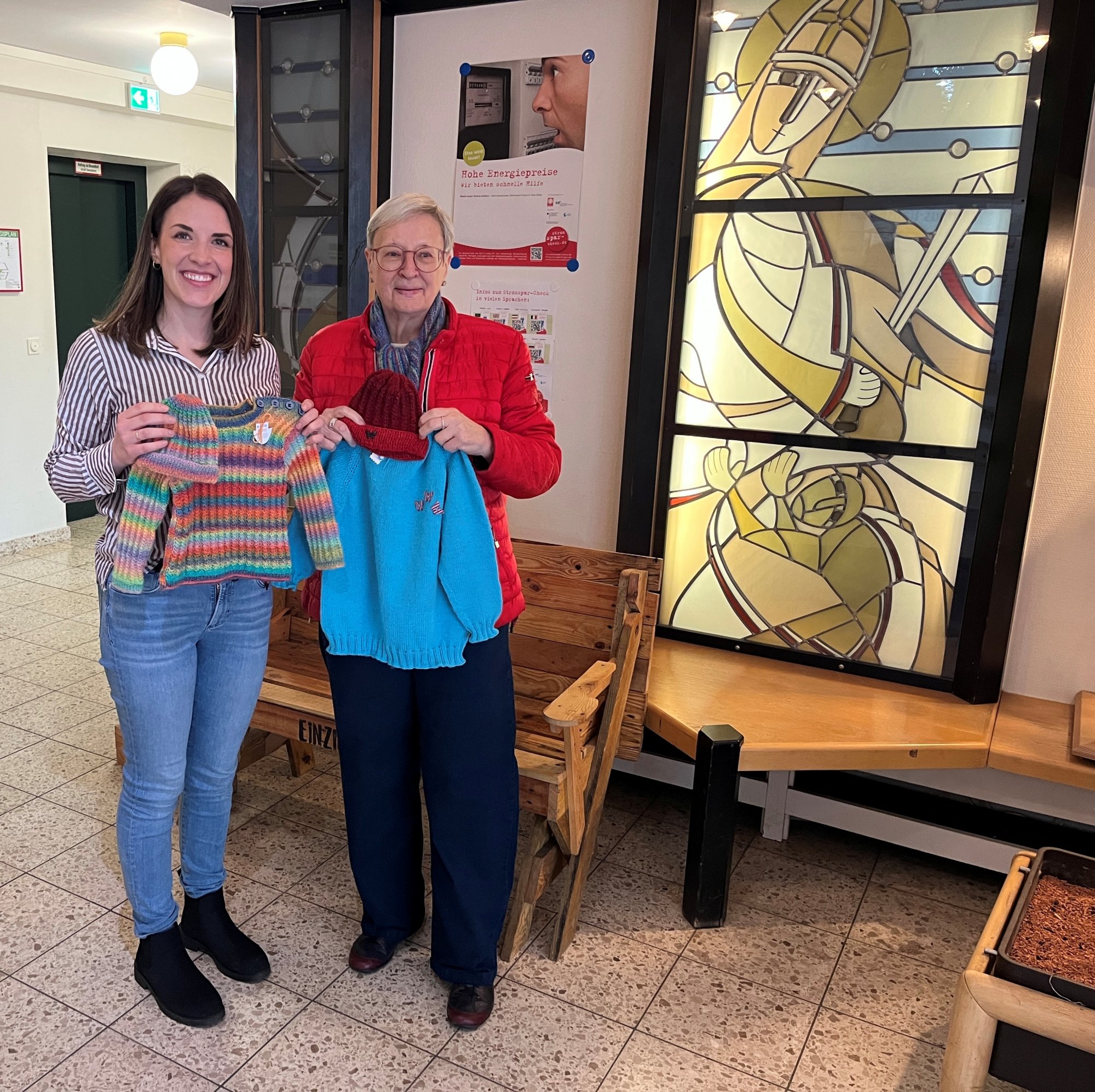 Zwei Personen sind abgebildet. Links, Frau Tomaszik vom Caritasverband und rechts Frau Walther vom DRK Lüdenscheid. Sie halten beide zwei selbstgestrickte Jacken hoch.