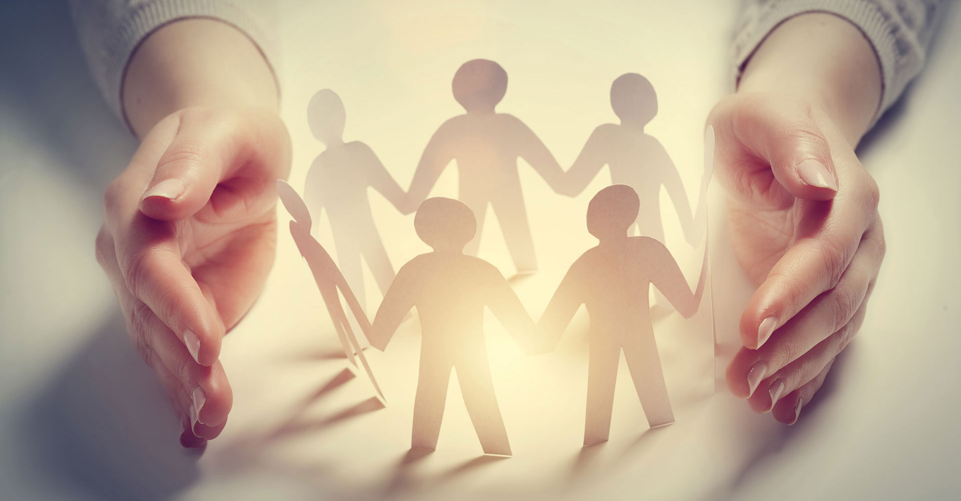 Zwei Hände umfassen schützend eine Kette aus Papierfiguren, die sich an den Händen halten.