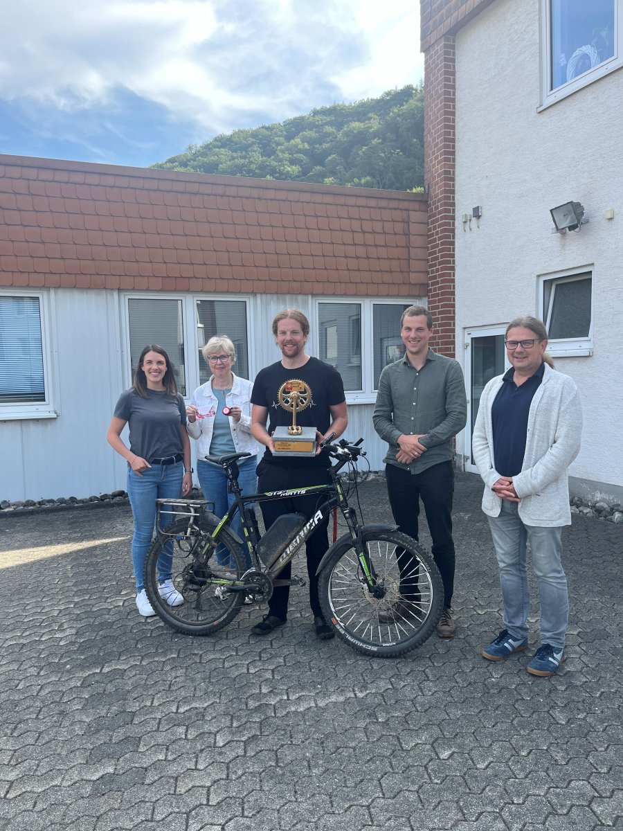 Gruppe vor Caritas-Einrichtung mit Fahrrad und Pokal bei einer Preisverleihung