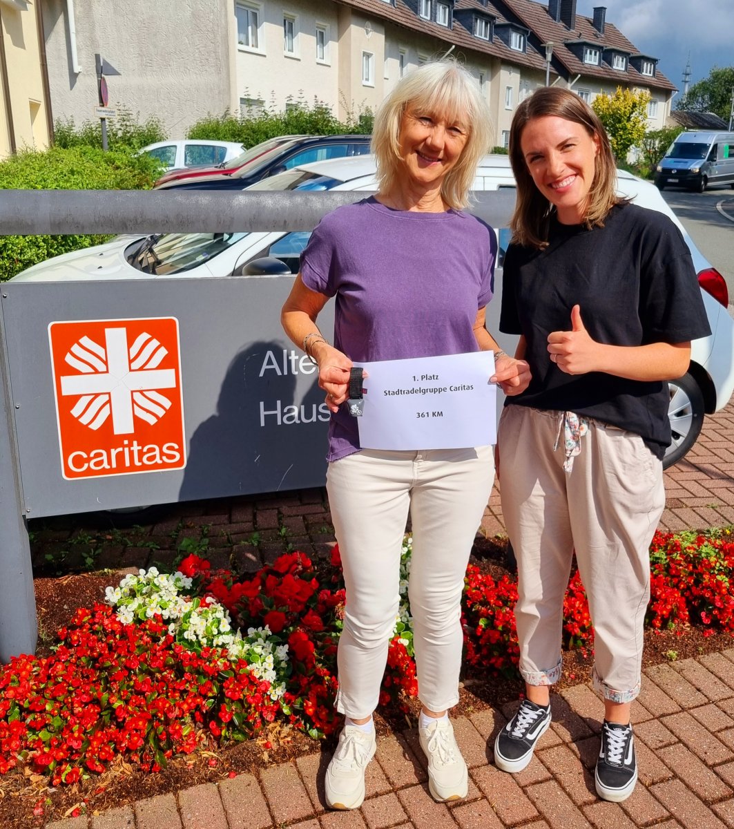 Zwei Caritas-Mitarbeiterinnen mit Urkunde ‚1. Platz Stadtradelgruppe Caritas – 361 km vor Caritas-Schild
