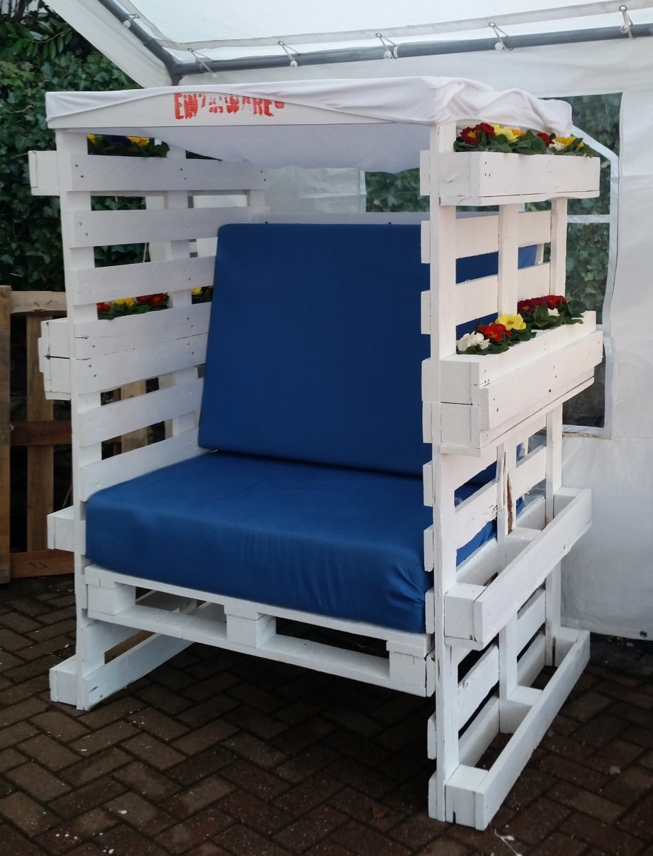 Sitzbank aus Paletten mit blauem Polster und Blumen in einem weißen Holzrahmen