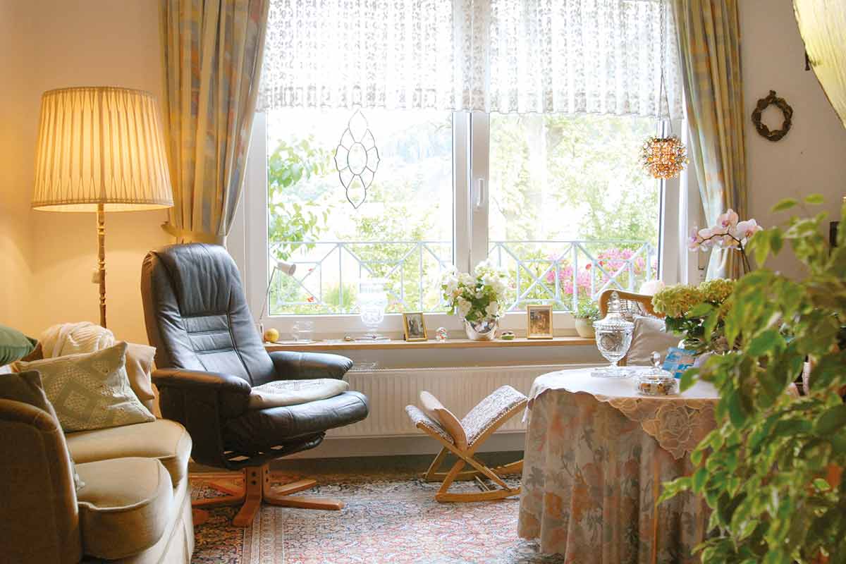 Heller Wohnraum mit Sofa, Sessel und großer Fensterfront in einer Seniorenwohnung